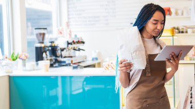 Kahvecide çalışırken gülümseyen bayan barista internetten sipariş veriyor. Elinde kahve çekirdekleri olan bir paket kağıt tutan kadın. Restoran yemekleri ve içki konsepti