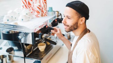 Kahve dükkanında müşterilere kahve hazırlayan mutlu erkek barista. Espresso yapıyorum, Americano. Küçük kahve işi.