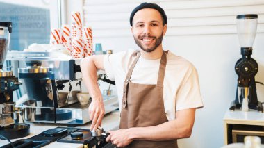 Gülümseyen barista kahve telvesini kurcalayıcı ile sıkıştırıyor. Kahve hazırlıyorum. Kahve dükkanında çalışan Barista.