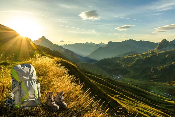 Hiking equipment in early morning sunrise and mountain silhouettes. Backpack and hike shoes in beautiful sunlight and sunbeams. Tyrol, Lechtal, Austria. Allgaeu, Alps.