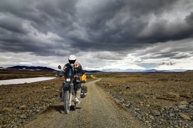 Lonely Motorbiker Man drives through icelandic Highland Landscape with Motorcycle and Travel Equipment on dirt road F550 in Kaldidalur, Iceland.