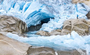 One Man standing in front of big Glacier Tongue and melt water river. Nigardsbreen, Jostedalsbreen National Park, Norway.