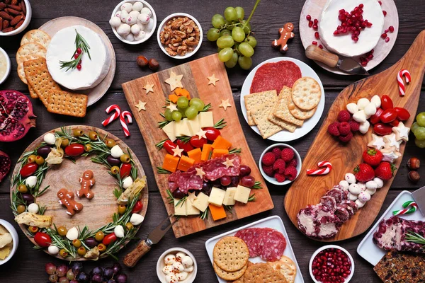 stock image Christmas charcuterie table scene against a dark wood background. Assortment of cheese and meat appetizers. Christmas tree, wreath and candy cane arrangements.