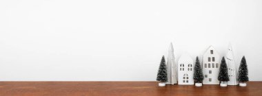 Ahşap bir rafta ağaçların olduğu beyaz bir Noel evi dekoru. Fotokopi alanı olan beyaz bir duvar afişi.