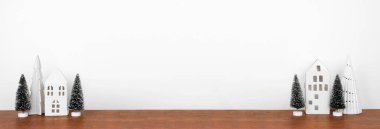 Ahşap bir rafta ağaçların olduğu beyaz bir Noel evi dekoru. Fotokopi alanı olan beyaz bir duvar afişi.