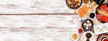 Yılbaşı temalı aperatifler yan sınırı. Beyaz ahşap bir arkaplanda manzaranın üstünde. Şarküteri tahtası, şampanya, saat kurabiyesi, smokin peyniri ve çeşitli parti yemekleri. Boşluğu kopyala.