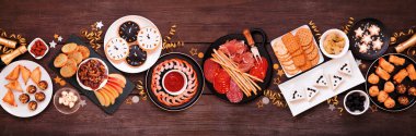 Yılbaşı temalı aperatif masası sahnesi. Koyu ahşap arka planda üst manzara. Şarküteri tahtası, şampanya, saat kurabiyesi, smokin peyniri ve parti yemekleri..