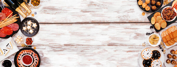 Новый год тема закуски двойной границы. Вид сверху на фоне белого деревянного знамени. Картонная доска, шампанское, часовые кулинарии, сыр тудо-бри и разнообразная праздничная еда. Копирование пространства.