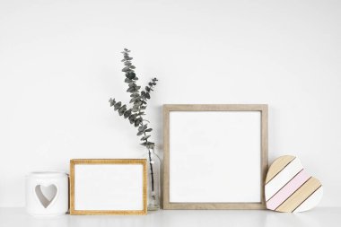 Mock up wood frames with rustic Valentines Day wooden heart decor, eucalyptus branch and candle holder. White shelf against a white wall. Copy space.
