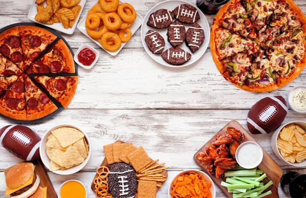 Super Bowl or football theme food side border. Pizza, hamburgers, wings, snacks and sides. Top down view on a white wood background.