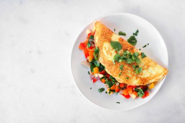 Healthy vegetable loaded omelette. Top view on a plate over a white marble background.