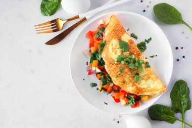 Healthy vegetable loaded omelette. Overhead view corner border on a white marble background.