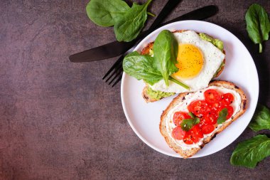 Healthy avocado egg and cream cheese tomato toasts. Top view table scene on a dark stone background