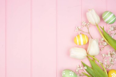 Pastel Easter eggs and white spring tulip flowers. Overhead view side border against a pink wood background. Copy space.