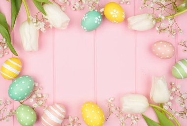 Pastel Easter eggs and white spring tulip flowers. Above view frame against a pink wood background. Copy space.