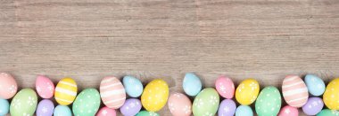 Colorful pastel Easter egg bottom border. Top down view on a light wood banner background. Copy space.