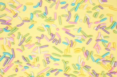 Colorful candy sprinkles background. Above view on a yellow background. Pastel Easter color theme.
