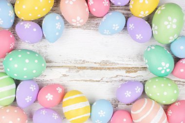 Pastel colored Easter egg frame. Overhead view over a rustic white wood background. Copy space.
