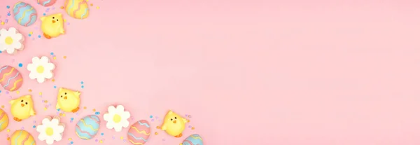 Easter candy corner border. Colorful pastel candy eggs, chicks and flowers. Above view side border against a pink banner background. Copy space.