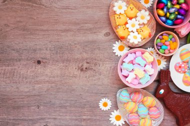 Easter candy side border. Above view over a wood background. Chocolate bunnies, candy eggs and a mixture of sweets. Copy space.