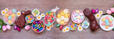 Easter candies. Overhead view table scene on a wood banner background. Chocolate bunnies, candy eggs and a collection of sweets.
