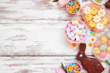 Easter candy side border. Above view over a white wood background. Chocolate bunnies, candy eggs and a variety of sweets. Copy space.