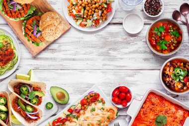 Healthy plant based vegetarian meal frame. Overhead view on a white wood background. Jackfruit tacos, zucchini lasagna, walnut bolognese zoodles, chickpea burgers, hummus, soups, salad.