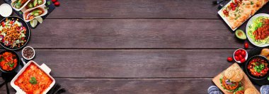 Healthy plant based vegetarian meal double border. Overhead view on a dark wood banner background. Jackfruit tacos, zucchini lasagna, walnut bolognese zoodles, chickpea burgers, hummus, soups, salad.