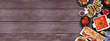 Healthy plant based vegetarian meal side border. Above view on a dark wood banner background. Jackfruit tacos, zucchini lasagna, walnut bolognese zoodles, hummus, soups, salad.