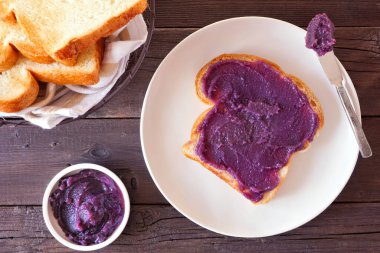 Ube halaya reçelli tost. Tatlı, modaya uygun, mor yer elması. Koyu ahşap arka planda en üstteki tablo sahnesi.