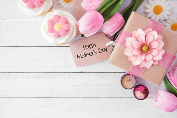 stock image Happy Mothers Day corner border with gift tag and box, flowers, cupcakes and chocolate. Overhead view against a white wood background. Copy space.