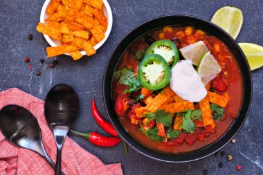 Domatesli tavuklu tortilla çorbası ve siyah fasulye. Meksika yemeği. Koyu arkaplanda en üstteki tablo sahnesi.