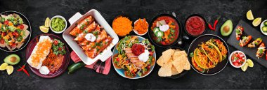 Meksika yemek masası sahnesi. Koyu taştan arka planda yukarıdan aşağıya doğru bir manzara. Taco, burrito tabağı, nachos, enchilada, tortilla çorbası ve salata..