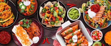 Meksika yemek masası sahnesi. Koyu ahşap bir arka planda tepeden aşağı manzara. Taco, burrito tabağı, nachos, enchilada, tortilla çorbası ve salata..