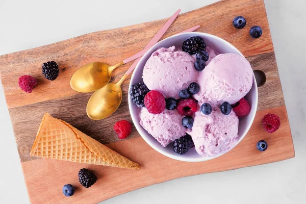 Bowl of field berry ice cream. Top down view table scene with a wooden serving board over a white marble background.