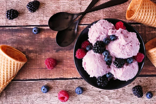 Bowl of field berry ice cream. Top view table scene over a wood background.