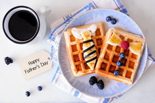 Fathers Day shirt waffles with necktie and bowtie with buttons. Homemade Fathers Day breakfast concept. Above view on a white marble background.