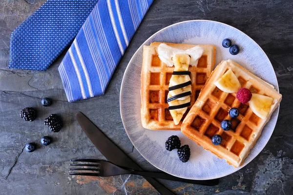 Fathers Day shirt waffles with necktie and bowtie with buttons. Homemade Fathers Day breakfast concept. Overhead view table scene on a dark slate background.