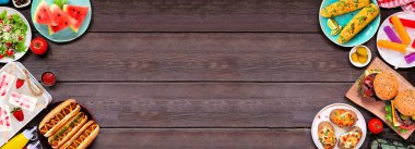 Yaz BBQ gıda çifte sınır. Hamburger, sosisli sandviç, patates, mısır ve soğuk ikramlar. Koyu ahşap bir arkaplanda manzaranın üstünde. Boşluğu kopyala.