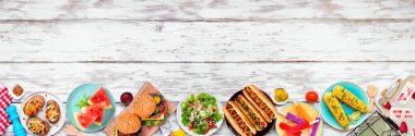 Yaz BBQ gıda alt sınırı. Hamburger, sosisli sandviç, patates, mısır ve soğuk ikramlar. Beyaz ahşap bir arka planda yukarıdan aşağıya doğru görünüyor. Boşluğu kopyala.