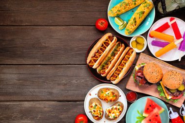 Barbekü ve gıda sınırında yaz tatili. Hamburger, sosisli sandviç, patates, mısır ve soğuk ikramlar. Koyu renk ahşap bir arka plan. Boşluğu kopyala.