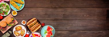 Yaz BBQ gıda köşe sınırı. Hamburger, sosisli sandviç, patates, mısır ve soğuk ikramlar. Koyu ahşap bir arka planda tepeden aşağı manzara. Boşluğu kopyala.