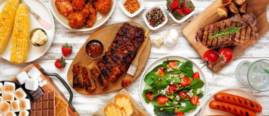Beyaz ahşap afiş üzerine yaz barbekü masası sahnesi. Izgara et, sebze tabağı ve bisküvi tabağı. Genel Görünüm.