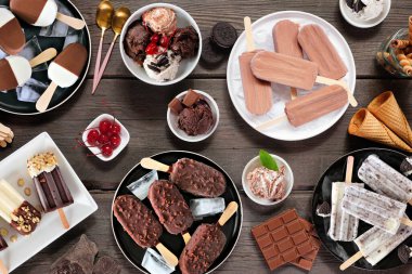 Harika bir yaz yemeği masası sahnesi. Çikolata temalı dondurma ve dondurulmuş şeker seçimi. Koyu ahşap arka planda üst görünüm.