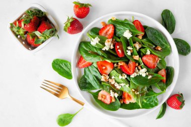 Yaz salatası ıspanak, çilek ve mavi peynir. Beyaz mermer bir arka planda yukarıdan görünen tablo sahnesi.