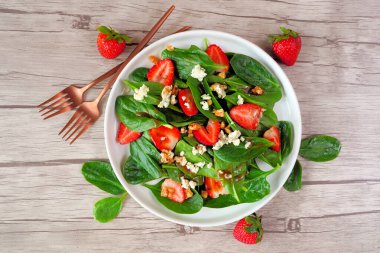 Yaz salatası ıspanak, çilek ve mavi peynir. Hafif ahşap zemin üzerinde malzeme çerçevesi olan üst görünüm.