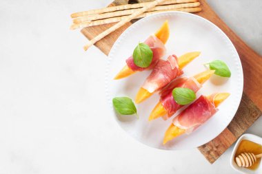 Prosciutto ve fesleğenli taze kavun. Beyaz mermer zemin üzerinde üst görünüm tablo sahnesi.