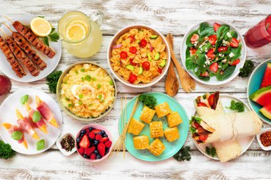 Beyaz ahşap arka planda yaz yemeği masası sahnesi. Ferahlatıcı salata, meyve, sargı bezi ve barbekü şişleri koleksiyonu. Üst görünüm.