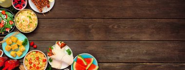 Koyu renk ahşap bir arkaplan üzerine yaz yiyecekleri köşesi sınırı. Çeşitli ferahlatıcı salatalar, meyveler, ambalajlar ve ızgara şişler. Yukarıdan aşağıya doğru. Boşluğu kopyala.