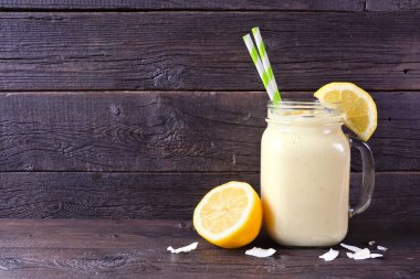 Limonlu, hindistan cevizli buzlu, mason kavanozlu ve dağınık malzemeli bir içecek. Koyu ahşap zemin ile yan görünüm.